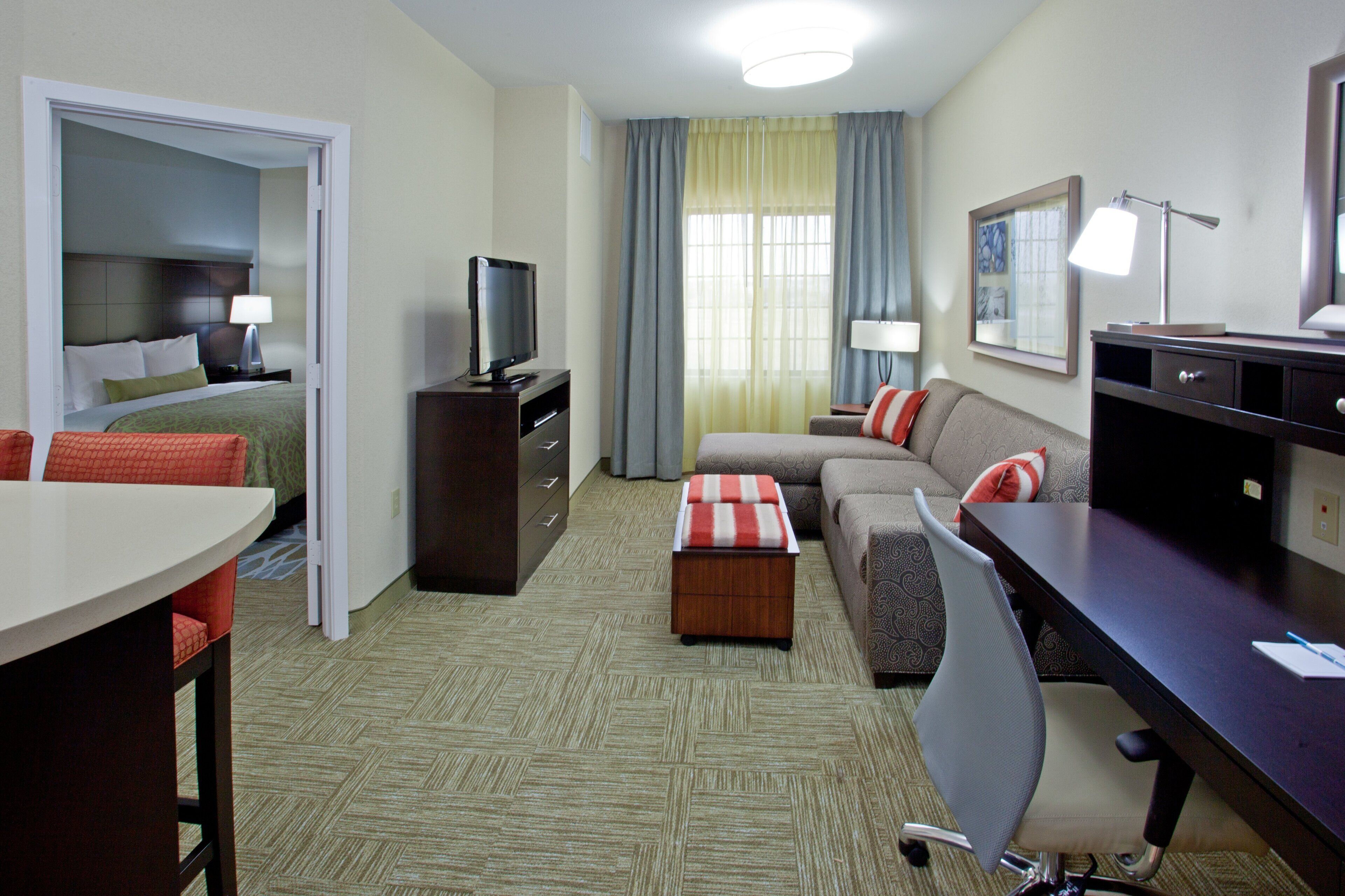Una habitación de hotel con cama, escritorio, silla, televisor y ventana con cortinas.