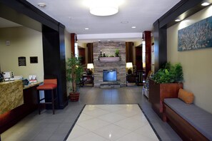 A hotel lobby with a reception desk, seating area, stone fireplace, and a large painting on the wall. - Staybridge Suites Houston Stafford - Sugar Land by IHG (Stafford)