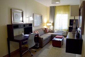 Quarto de hotel com escrivaninha, cadeira, sofá e televisão.