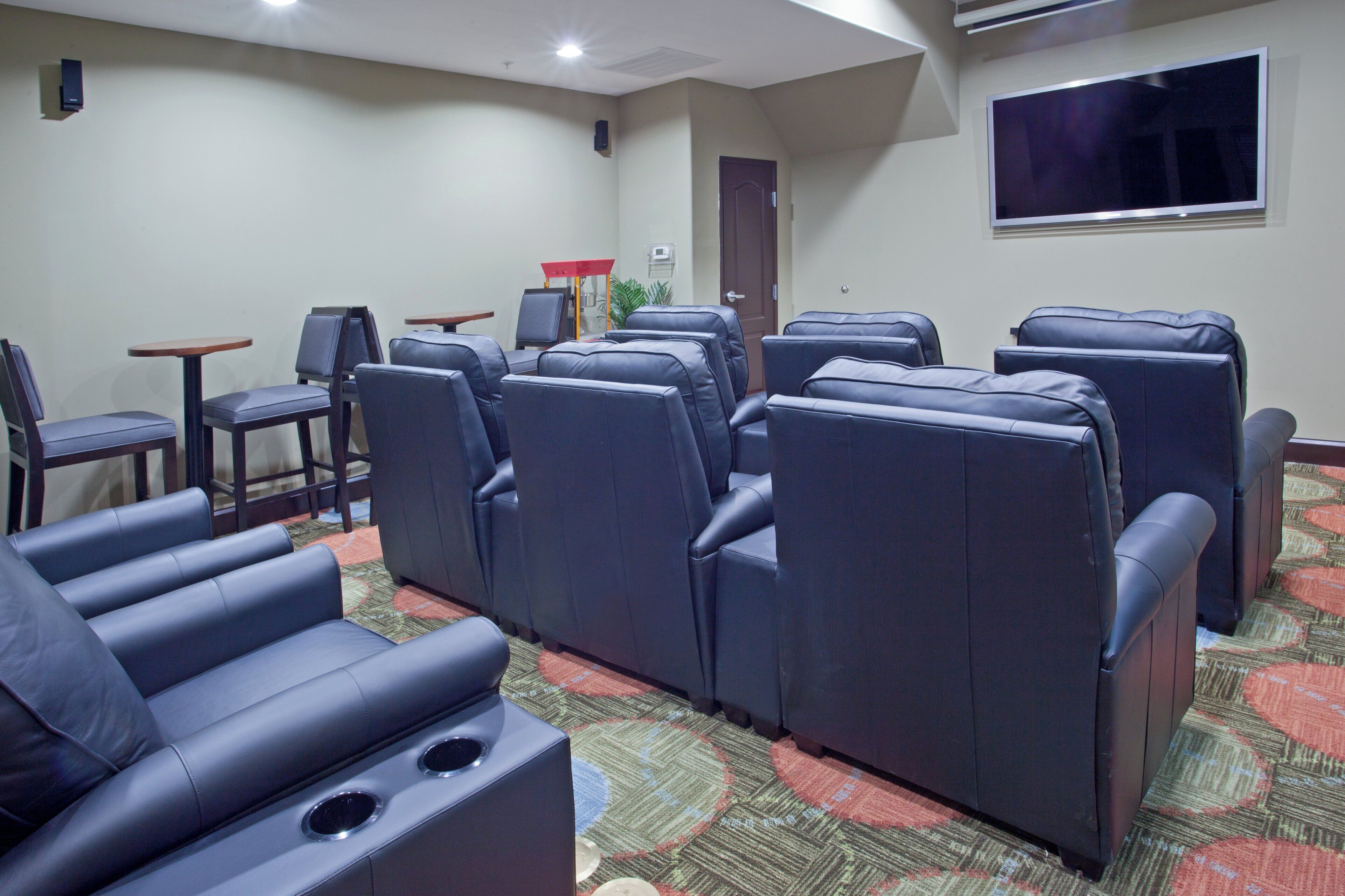 A conference room with rows of black leather chairs, a large flat-screen TV mounted on the wall, and a door in the background.