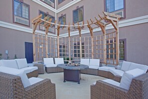 A covered outdoor seating area with wicker furniture and a central fire pit. - Staybridge Suites Houston Stafford - Sugar Land by IHG (Stafford)