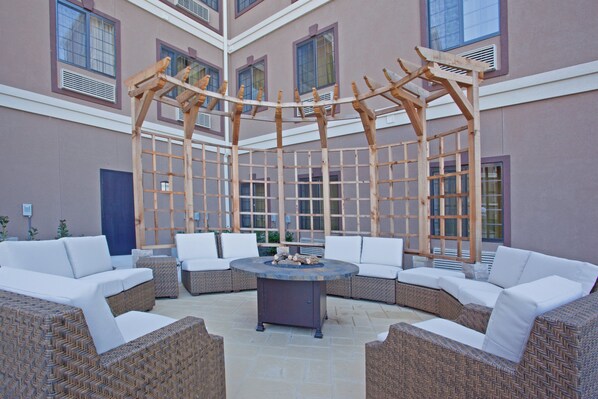A covered outdoor seating area with wicker furniture and a central fire pit. - Staybridge Suites Houston Stafford - Sugar Land by IHG (Stafford)