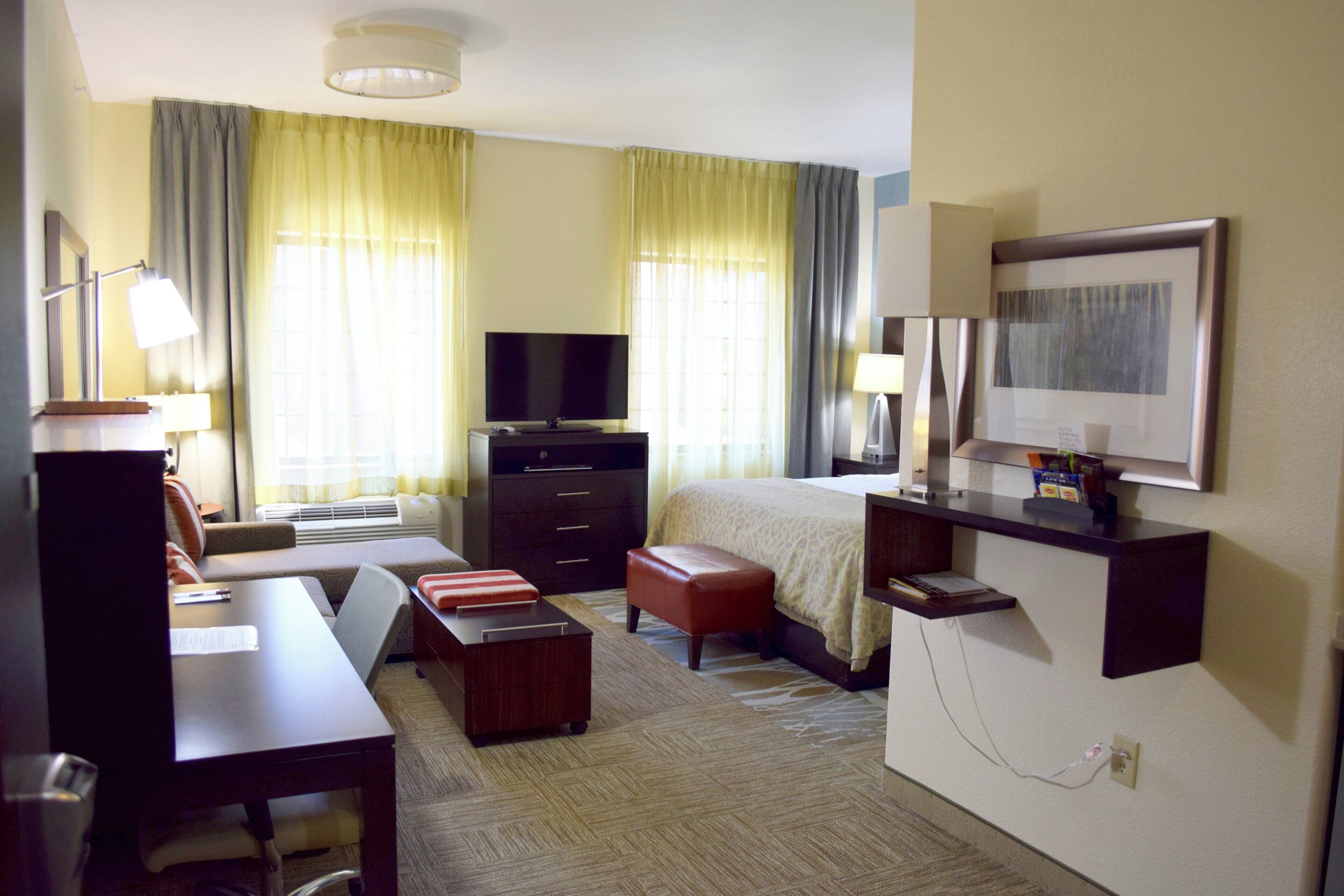 Habitación de hotel con cama, escritorio, silla, televisor y un cuadro en la pared.