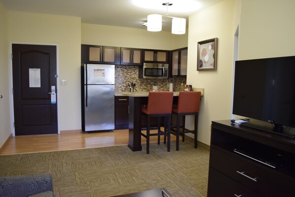 A compact kitchen with a refrigerator, microwave, and two bar stools. - Staybridge Suites Houston Stafford - Sugar Land by IHG (Stafford)