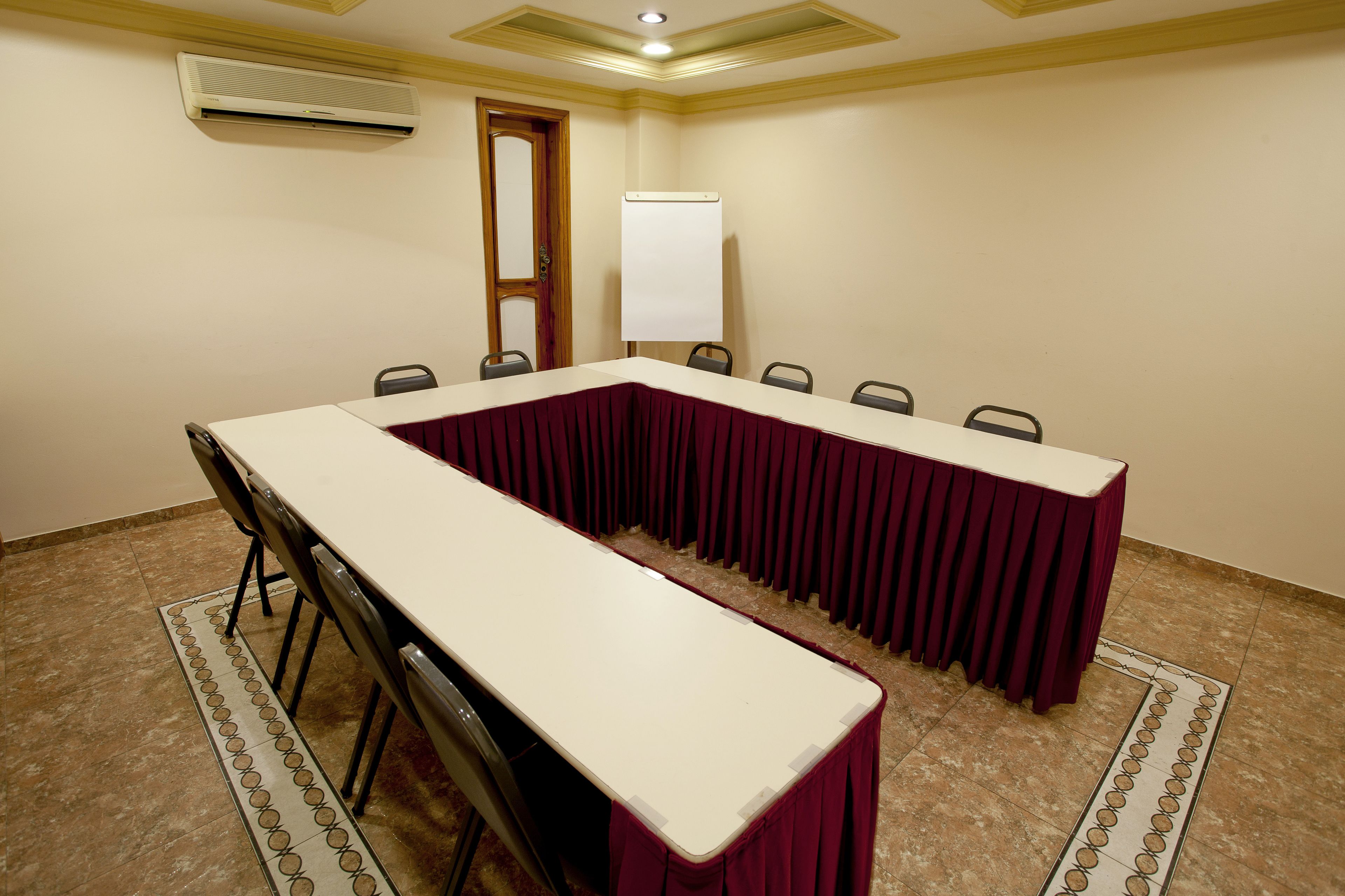 Un salón de conferencias con una larga mesa, sillas, una pizarra y un equipo de aire acondicionado.