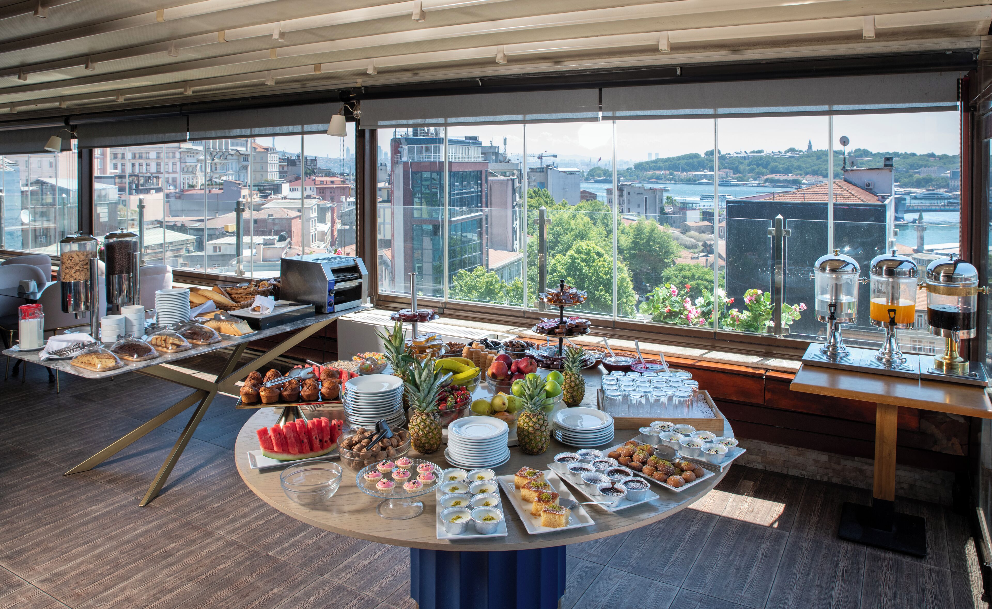 A breakfast buffet with a variety of foods and beverages, set against a city view.