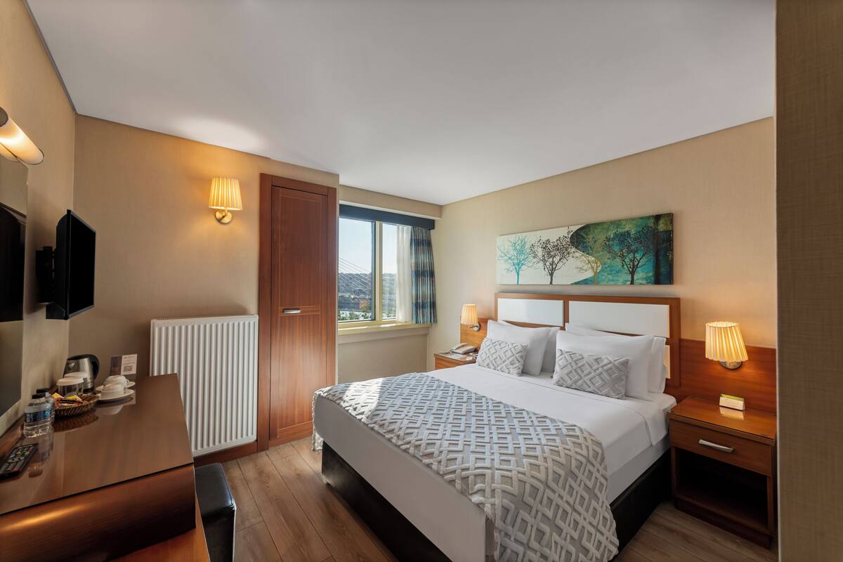 Ein Hotelzimmer mit einem Bett, Nachttischlampen, einem Fernseher, einem Schreibtisch und einem Fenster mit Vorhängen.