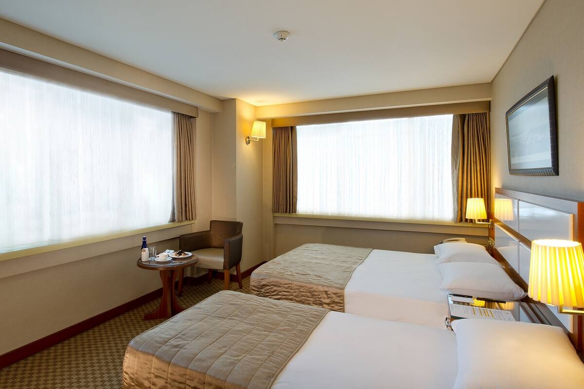 Ein Hotelzimmer mit zwei Betten, einem kleinen Tisch mit Stuhl und einem Fenster mit Vorhängen.