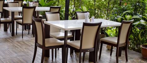 Un restaurante con mesas y sillas dispuestas al aire libre, rodeado de follaje.