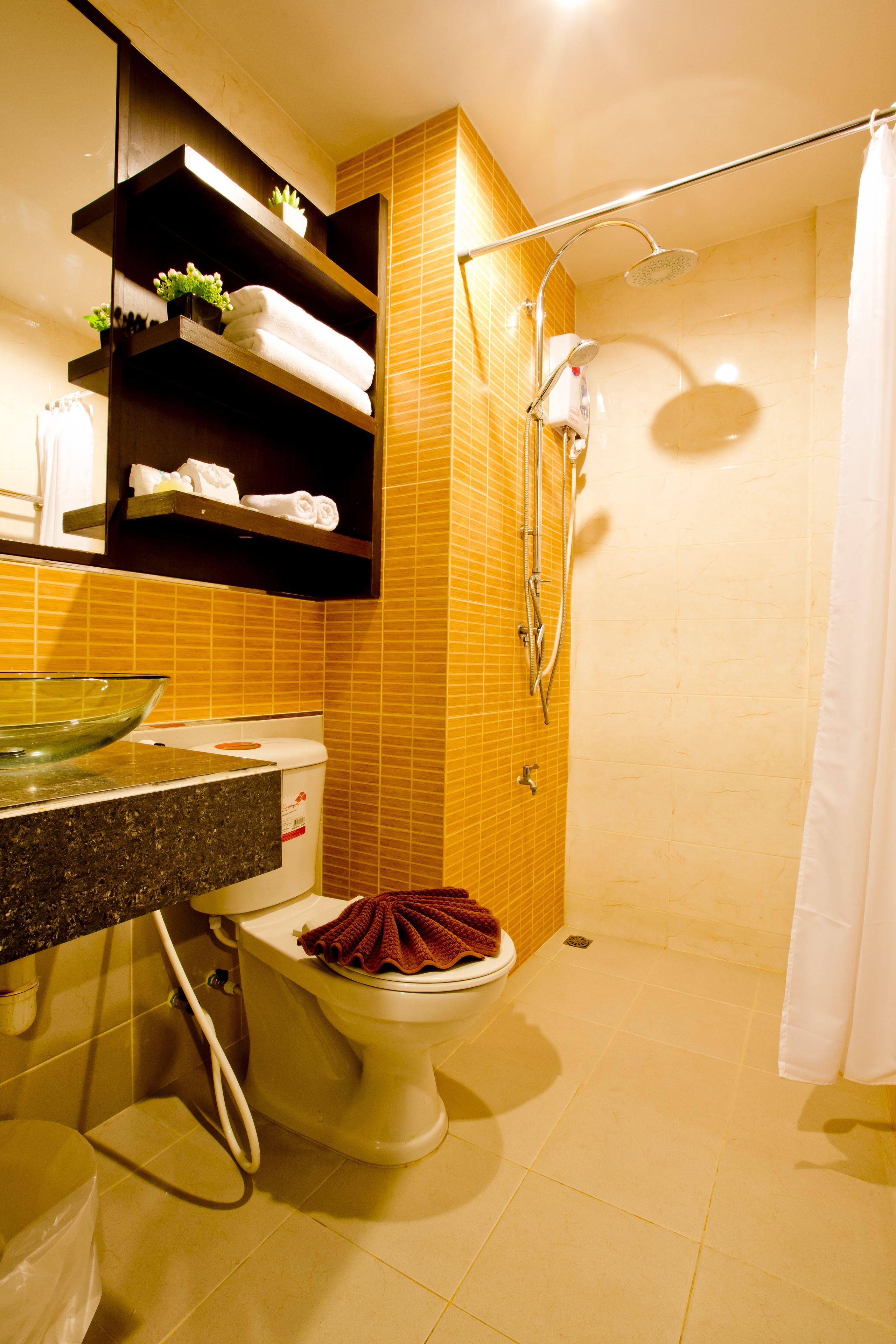 A bathroom with a toilet, a glass bowl sink, a shower, and a towel rack with towels.