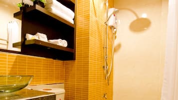 A bathroom with a toilet, a glass bowl sink, a shower, and a towel rack with towels.