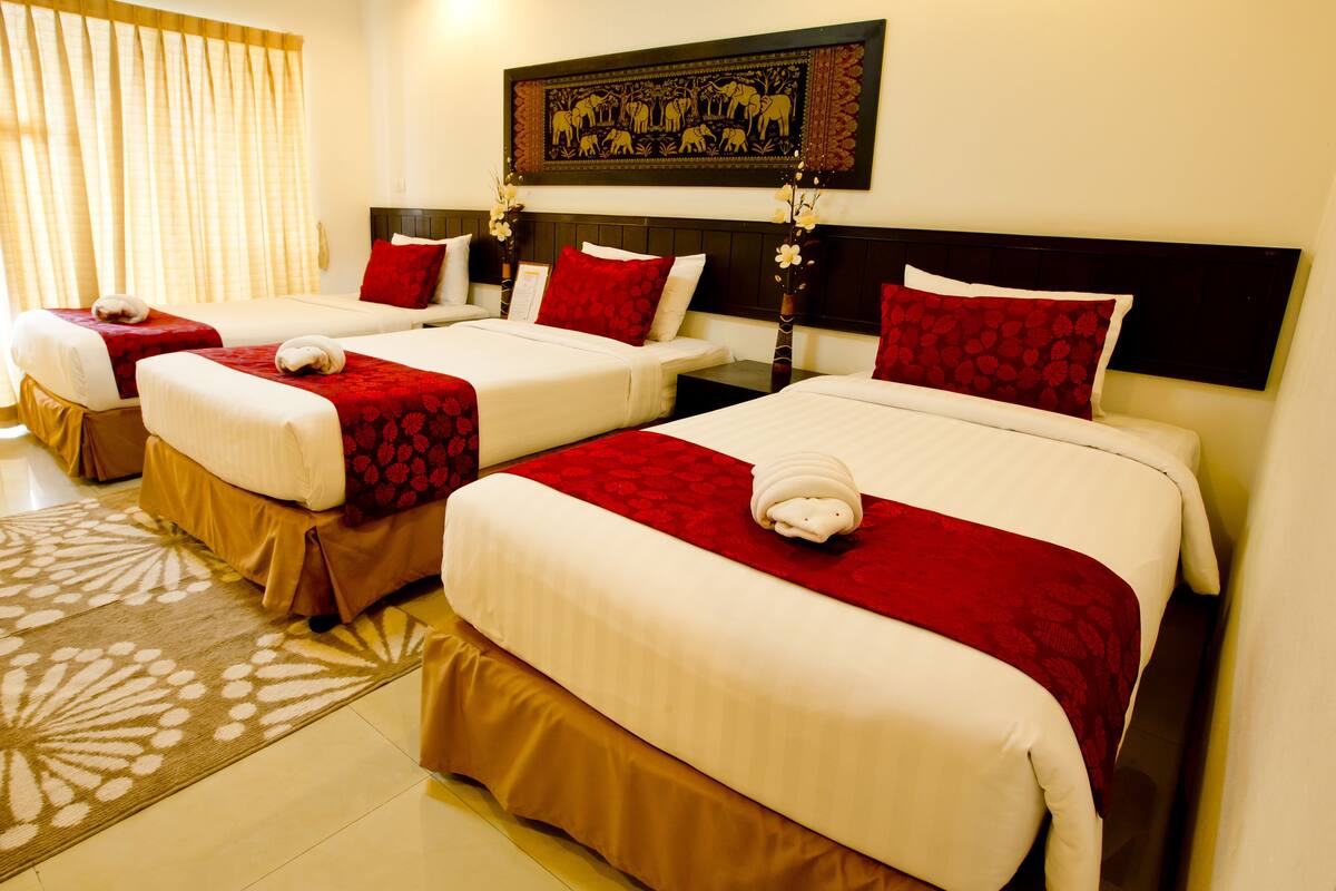 A hotel room with two beds, each with red and white bedding, a patterned rug, and a decorative wall hanging.