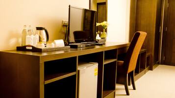 A hotel room with a desk, a chair, a television, a small refrigerator, and a trash bin.