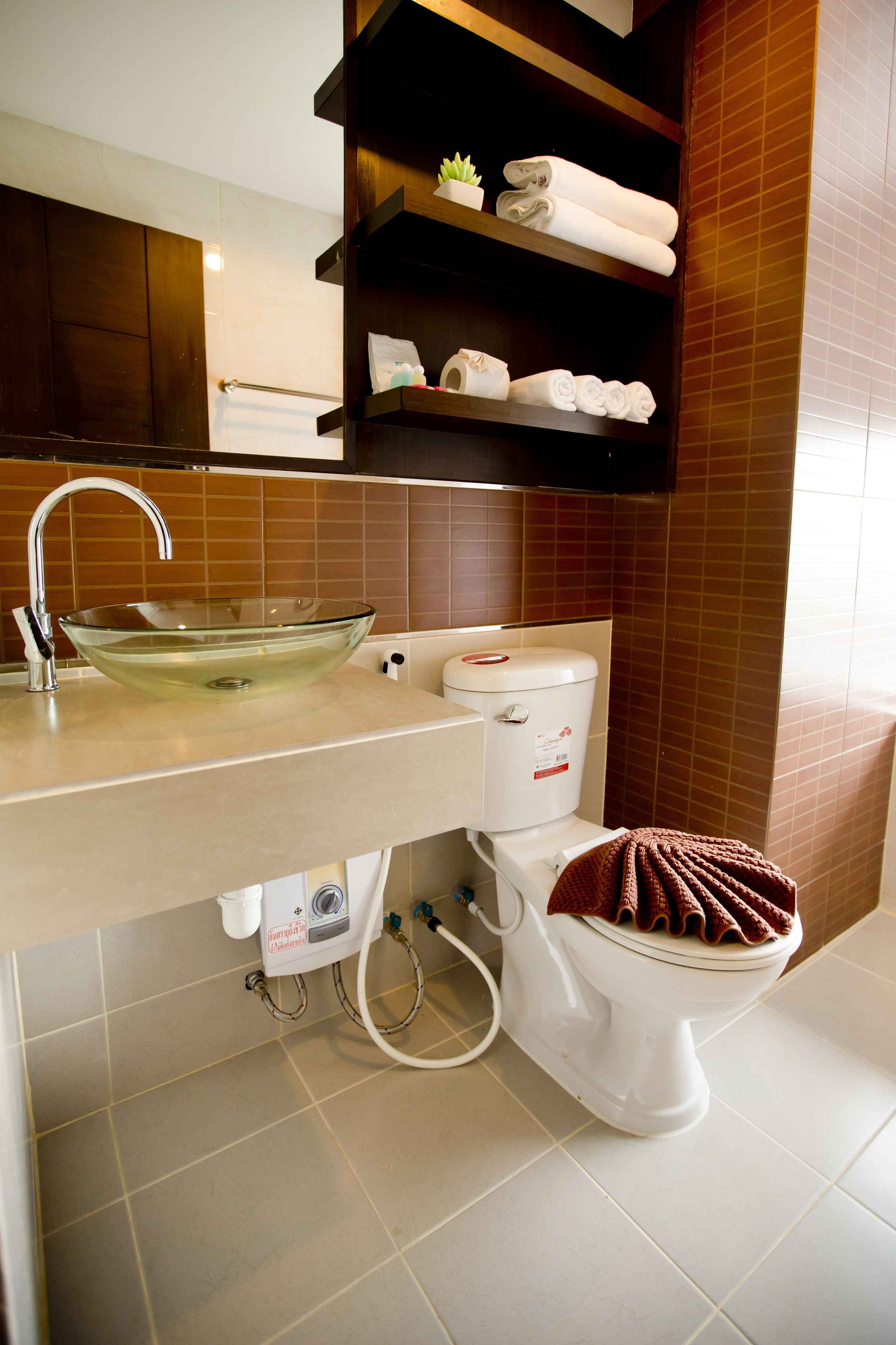Un baño con un lavabo de vidrio, un inodoro y un estante con toallas.