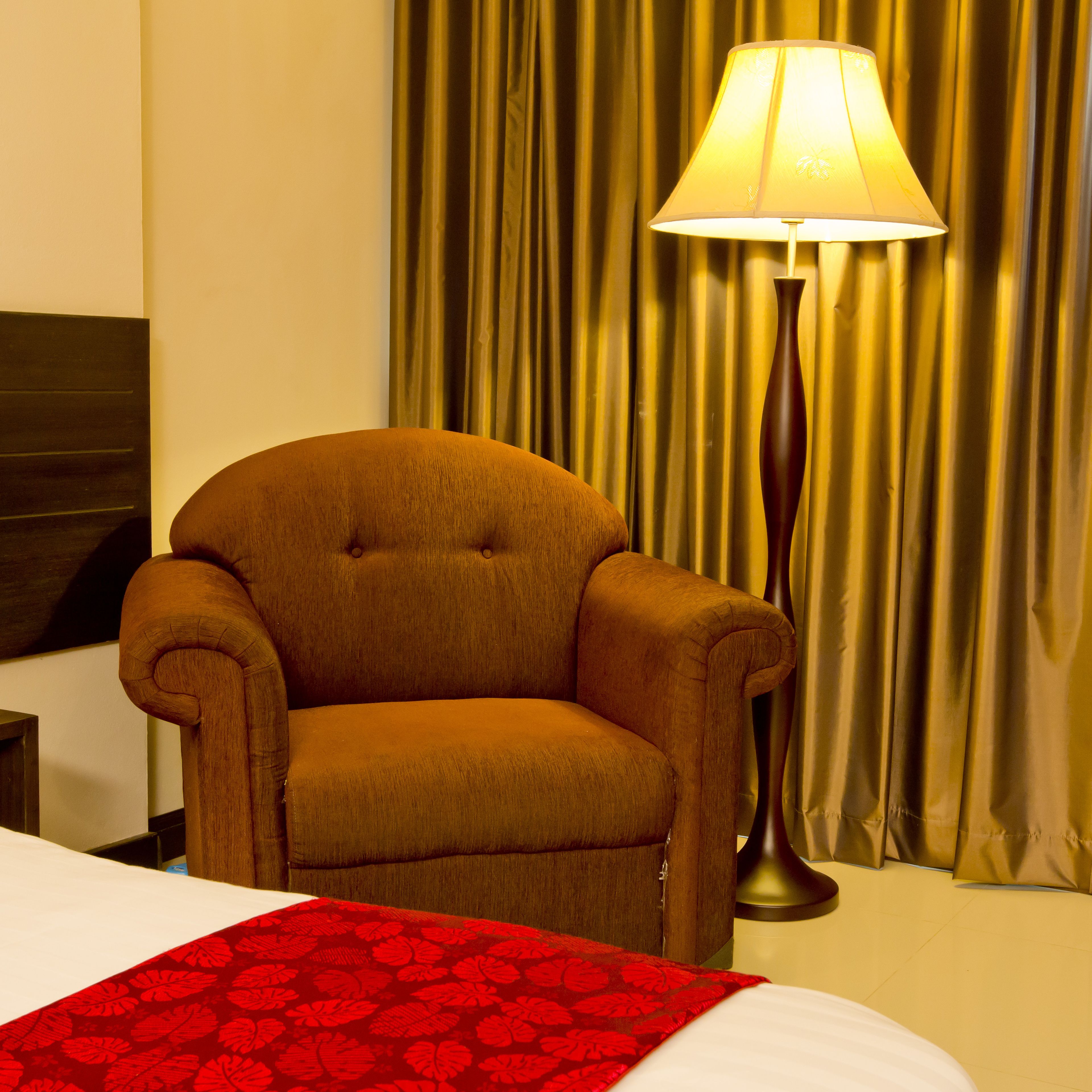 Een hotelkamer met een bed, een bruine fauteuil, een lamp en een gordijn.