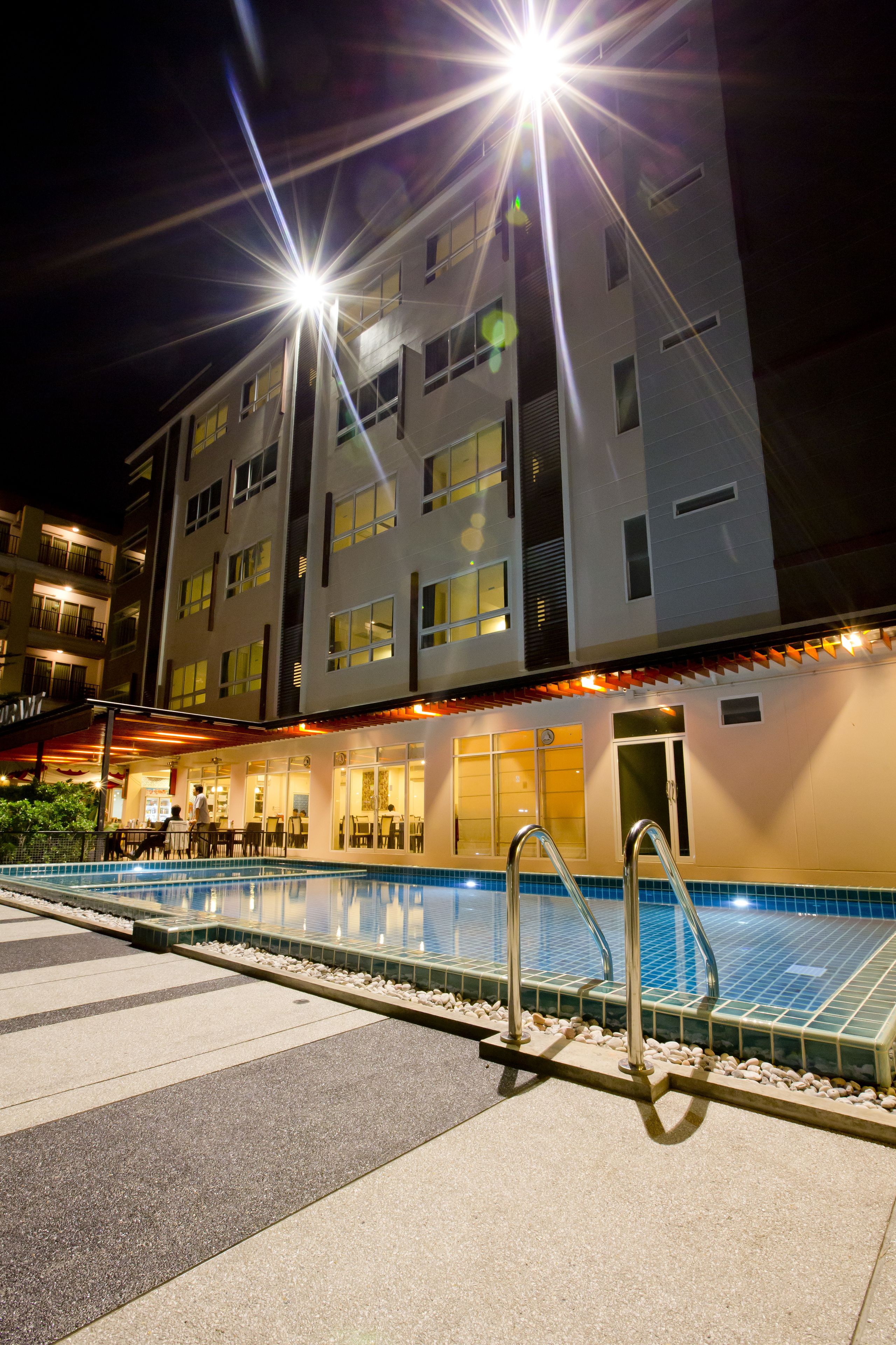 Ein Hotel bei Nacht mit Schwimmbad, Außenbereich mit Sitzgelegenheiten und mehreren Balkonen.