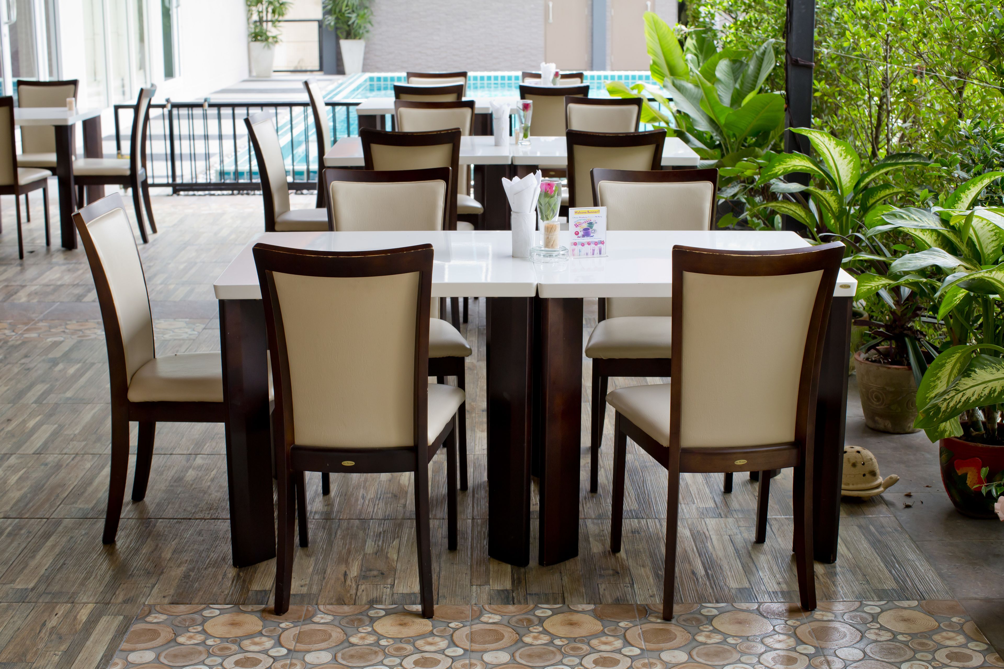 A restaurant with multiple tables and chairs, a tiled floor, and potted plants.