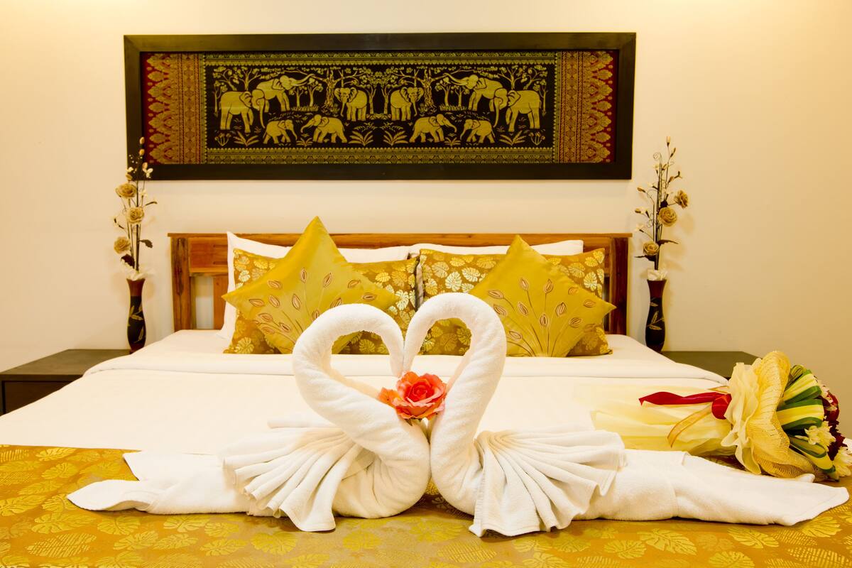 A hotel room with a bed, two pillows, a bouquet, and a wall decoration.