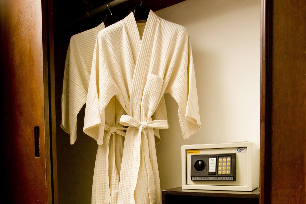 A wooden wardrobe with a robe hanging on the door and a pair of slippers on the shelf.
