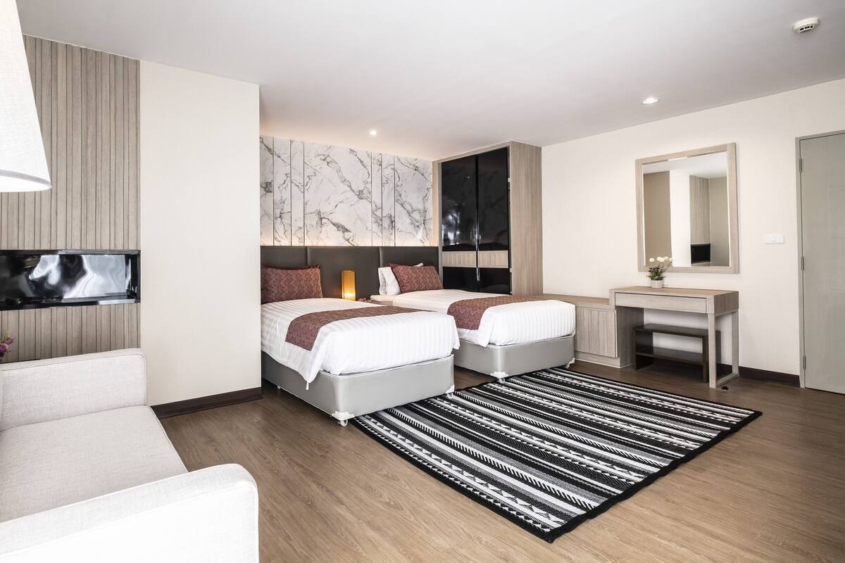 A modern hotel room with two beds, a desk, a TV, and a large mirror.