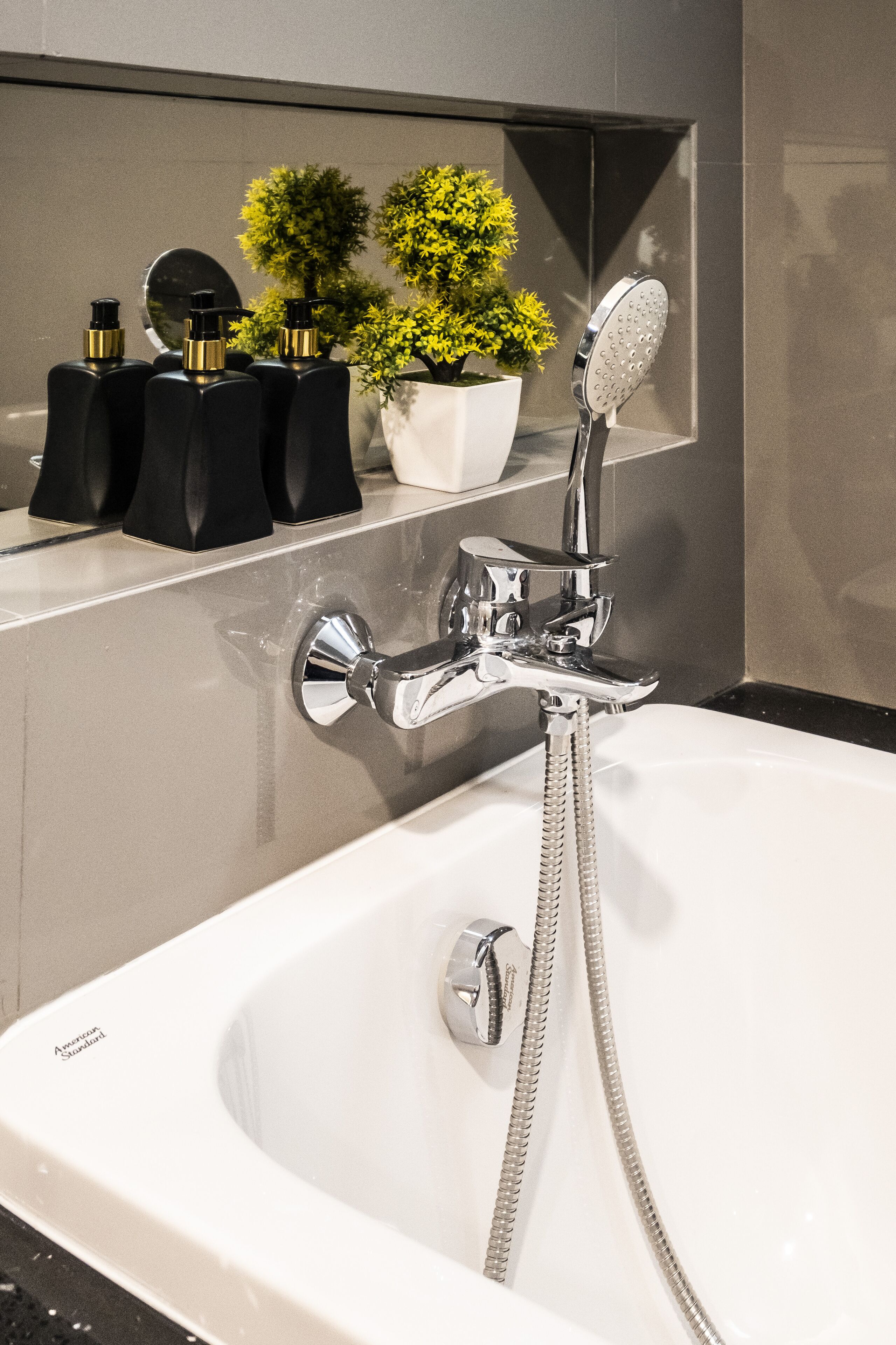 Un baño moderno con una bañera grande, un cabezal de ducha manual y una planta en maceta sobre una estantería.