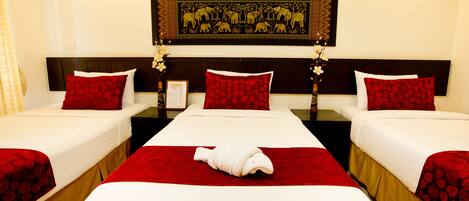 A hotel room with three beds, each with red floral bedding, a central bed with a towel, and a decorative wall hanging above.