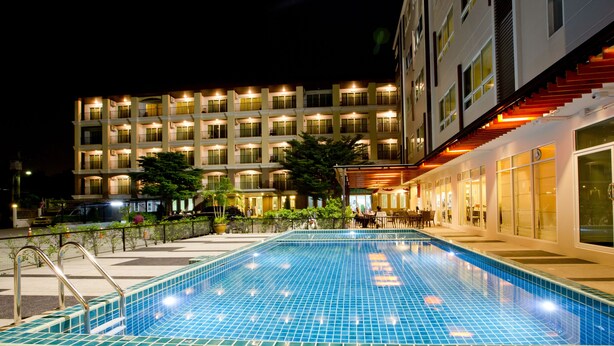 Een hotel met een zwembad, terras en een goed verlichte gevel.