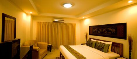 A hotel room with a bed, a sofa, a TV, and an air conditioning unit.
