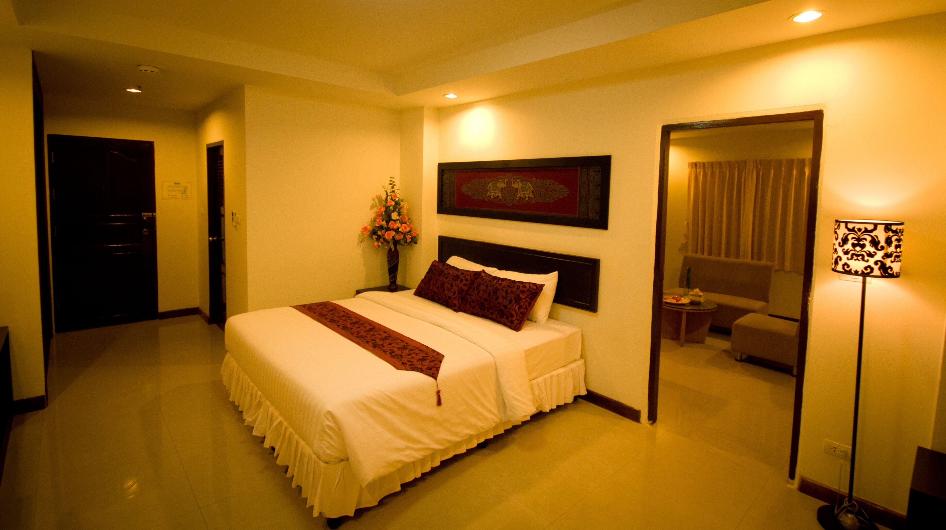 Habitación de hotel con una cama grande, una mesita de noche, una lámpara, un cuadro en la pared y una puerta que da a otra habitación.