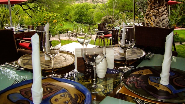 An outdoor dining area with tables set for two, featuring clear glassware and plates with a unique design. - Nirvana Restaurant And Retreat (San Miguel de Allende)