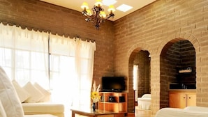 A living room with a brick wall, a chandelier, a sofa, a TV, and a fireplace. - Nirvana Restaurant And Retreat (San Miguel de Allende)