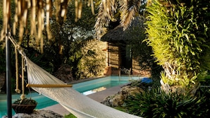 A hammock over a pool with a thatched-roof structure and lush greenery in the background. - Nirvana Restaurant And Retreat (San Miguel de Allende)