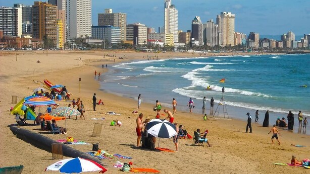 Una playa con sombrillas, gente y el horizonte de una ciudad al fondo.