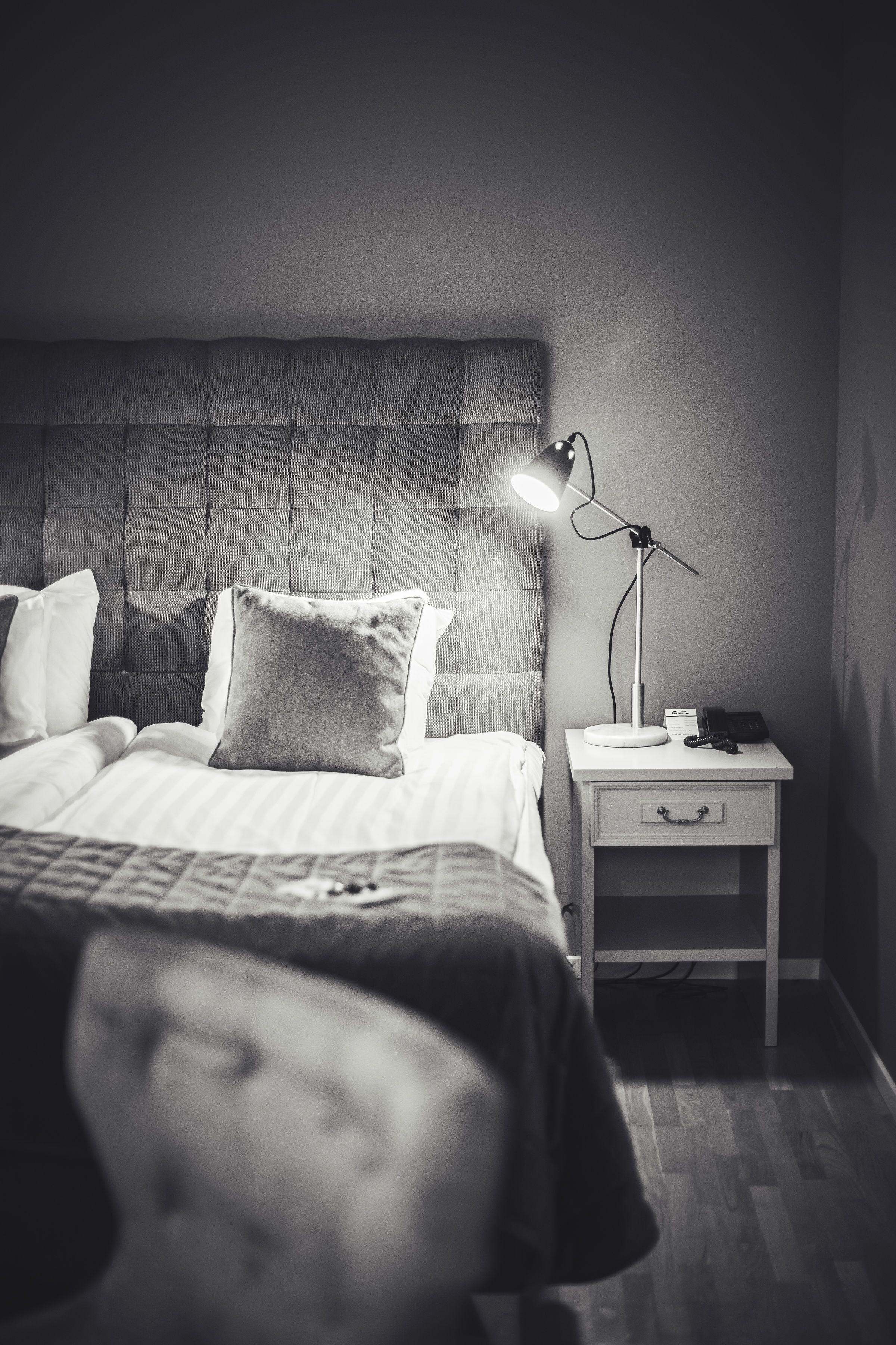 A neatly made bed with a headboard, a bedside lamp, and a small bedside table with a drawer.
