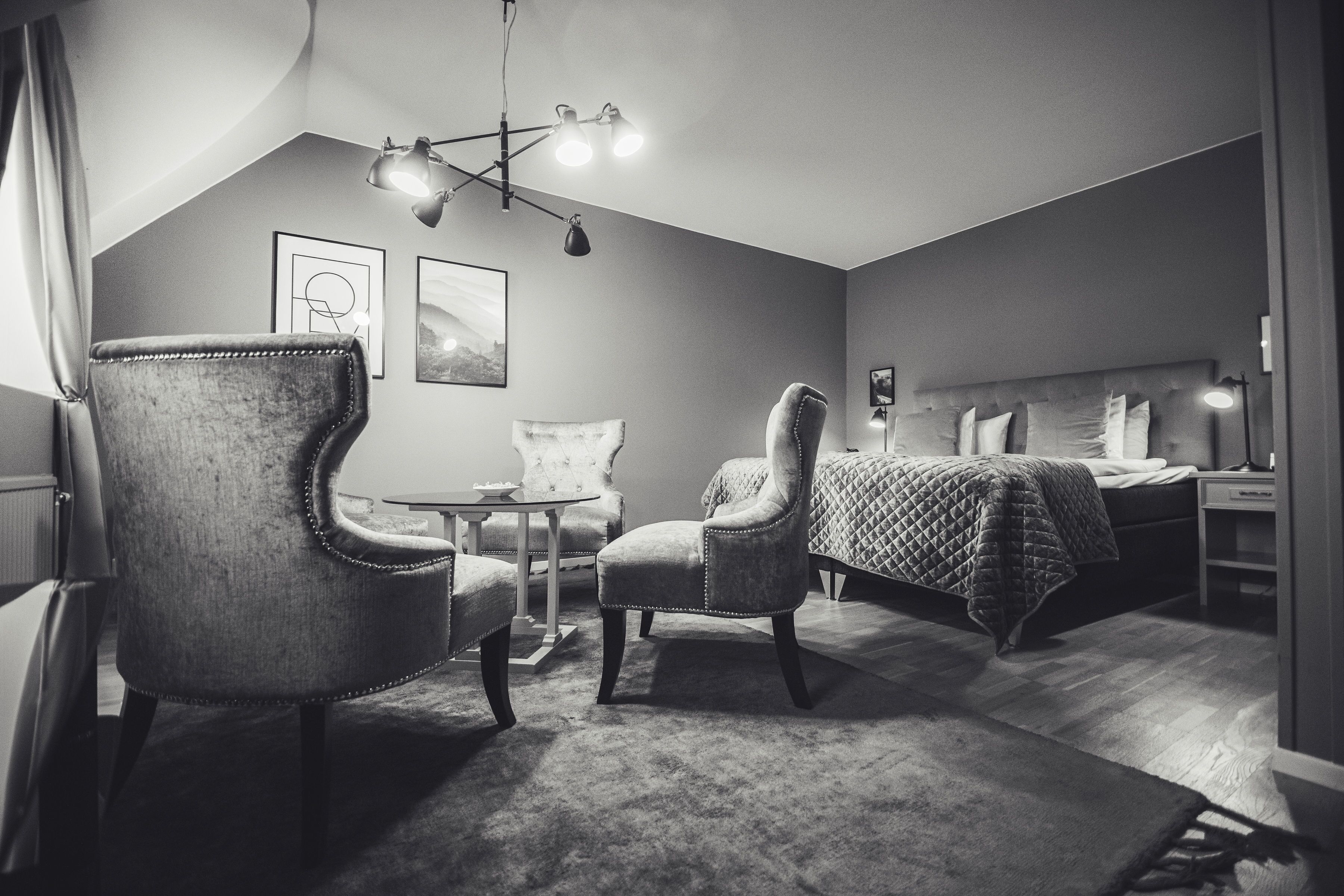 Ein modernes Schlafzimmer mit einem großen Bett, zwei Sesseln, einem kleinen Tisch und einer hängenden Leuchte.