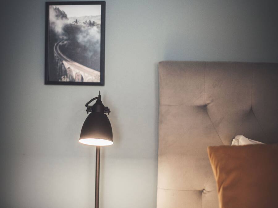 A neatly made bed with a headboard, a bedside lamp, and a framed picture on the wall.