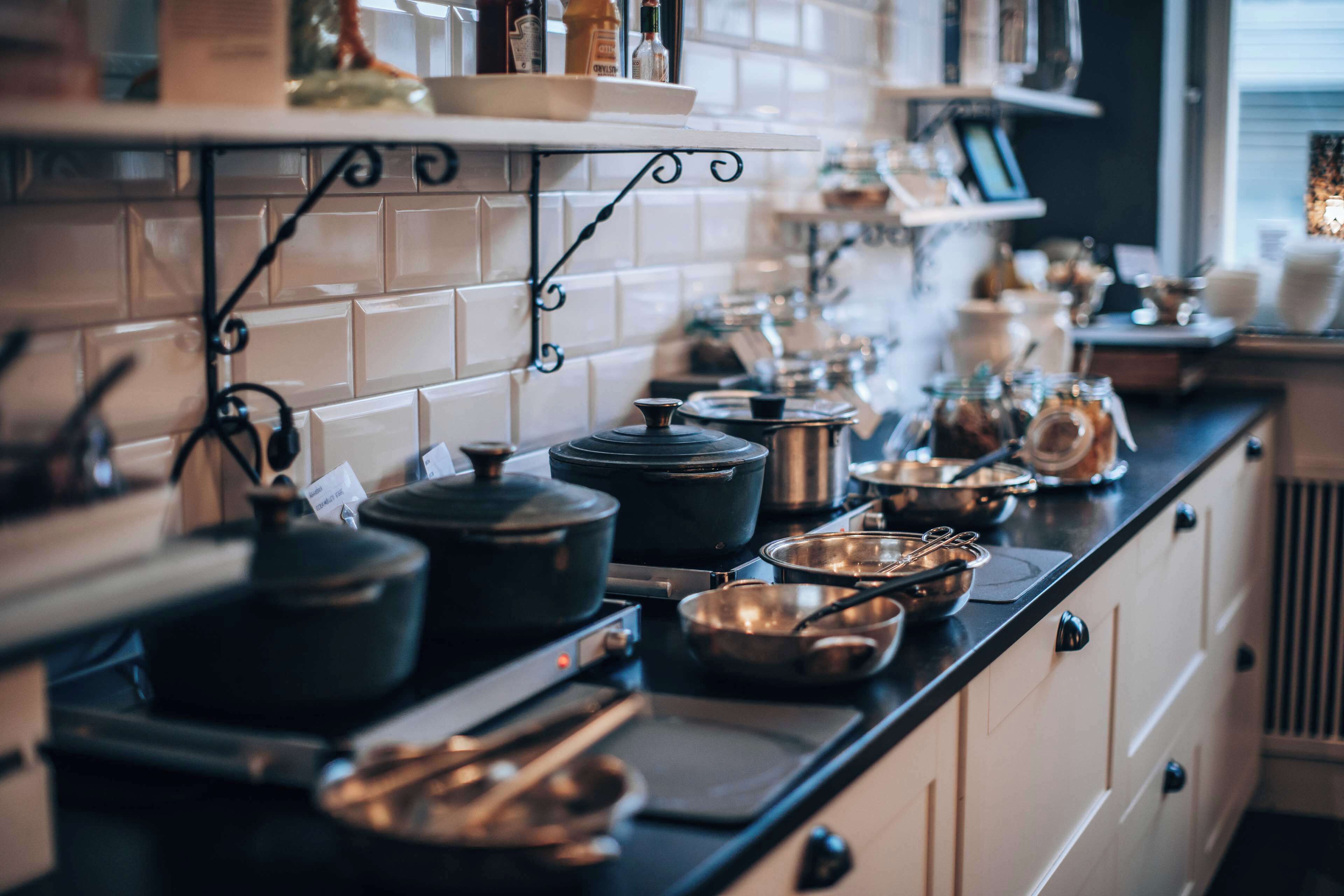 A kitchen with a black countertop, white cabinets, and various cooking utensils and pots.