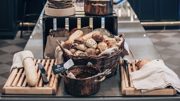 Una mesa de buffet con varios panes y pasteles, un cuchillo y una cesta de pan.