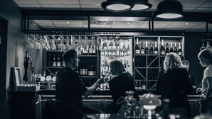 Una zona de bar con copas y botellas de vino colgando, una barra y estantes llenos de botellas.