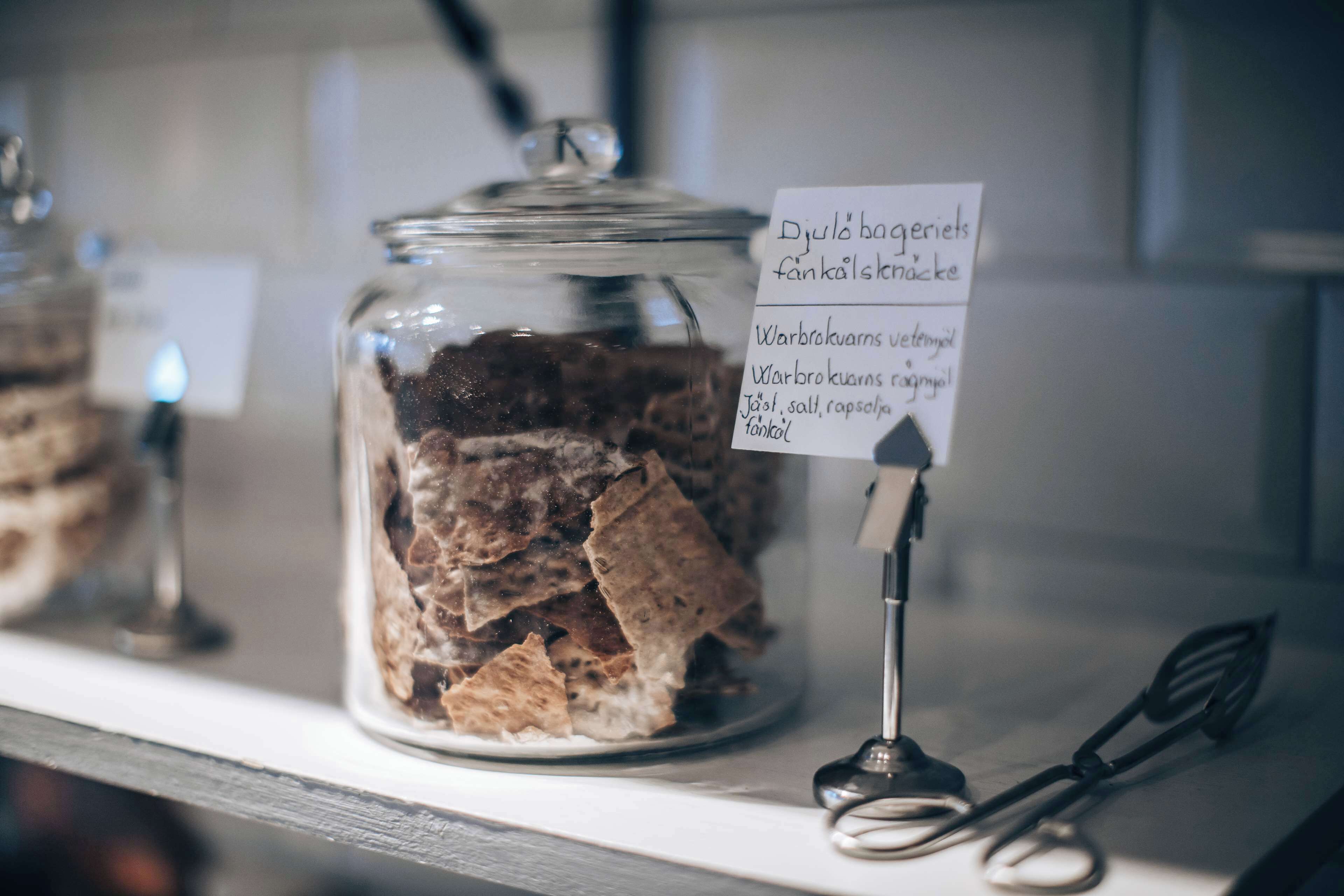 A glass jar filled with brown items, possibly snacks, with a sign listing ingredients.