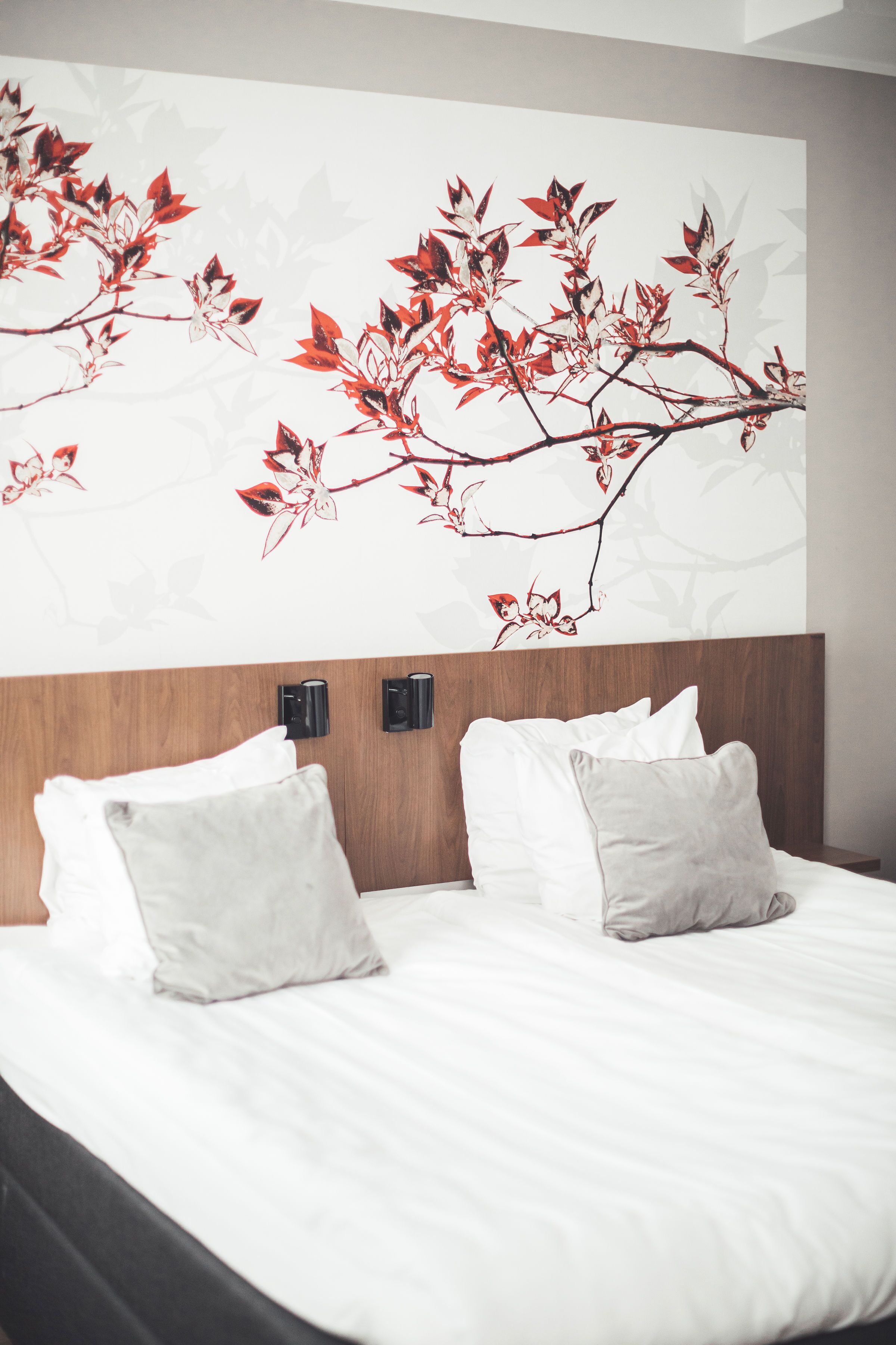 Una cama bien hecha con ropa de cama blanca y dos almohadas, un cabecero de madera y una pared con diseño floral.