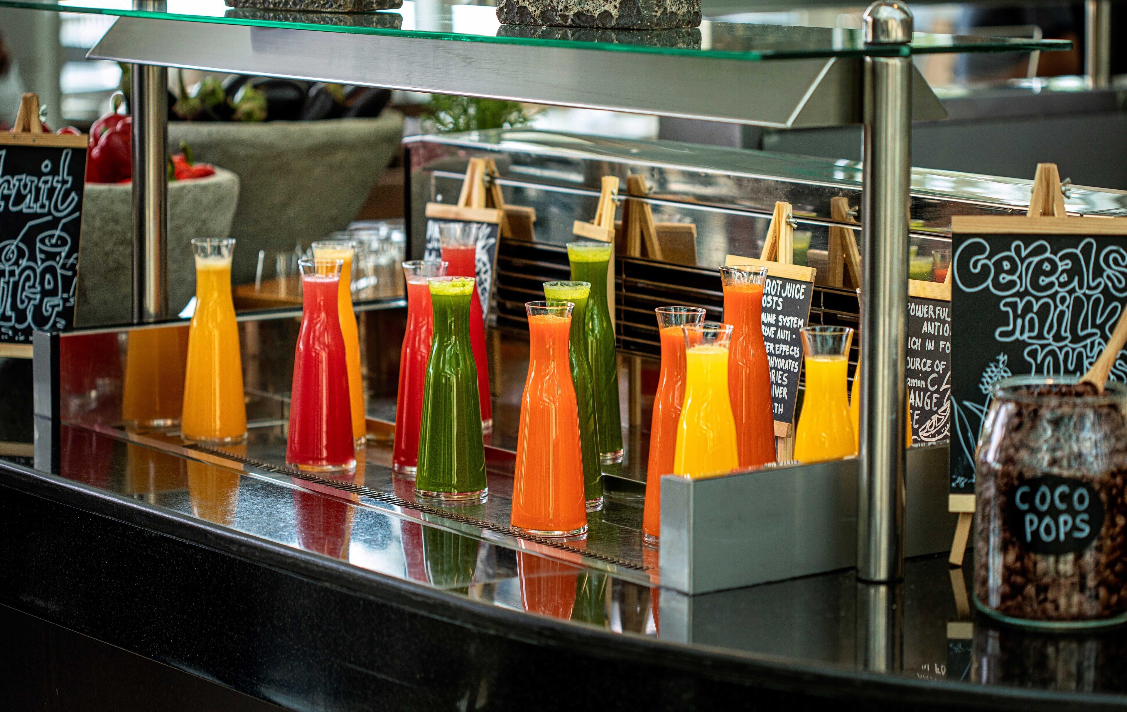 Un bar de zumos con diversas bebidas de colores y un cartel que dice 'Cereales Leche Coco Pops'.