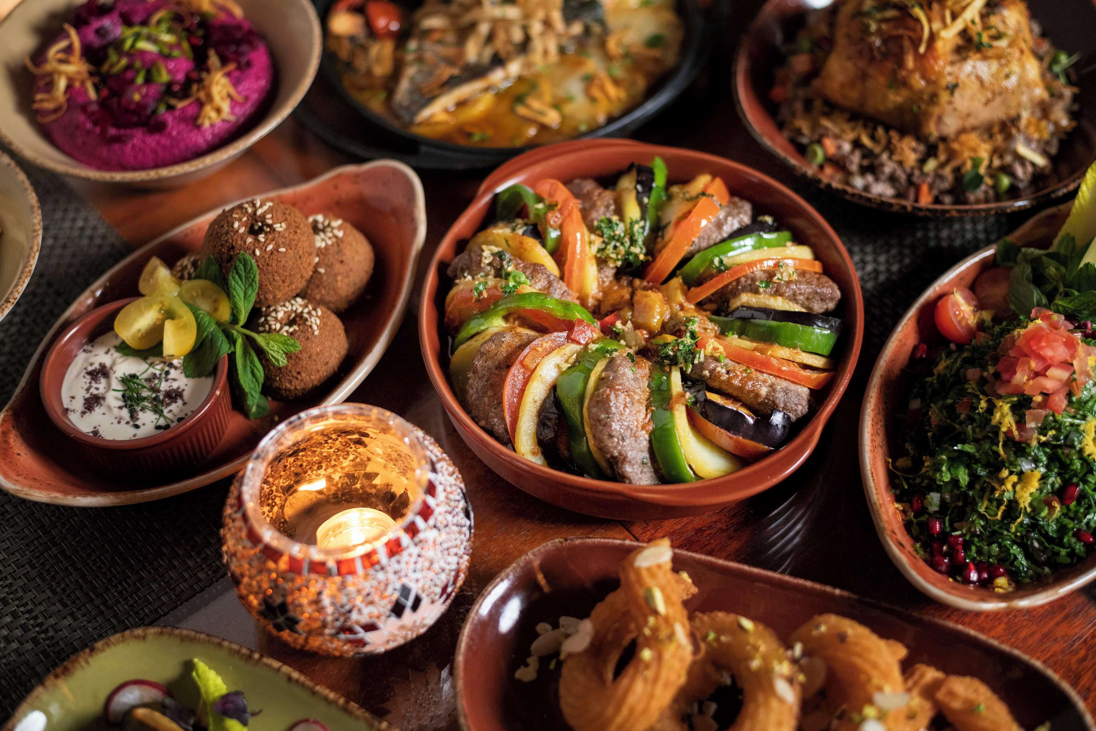 Variedad de platos, entre ellos un tazón de hummus, un plato de verduras rellenas y un guiso de pollo asado.