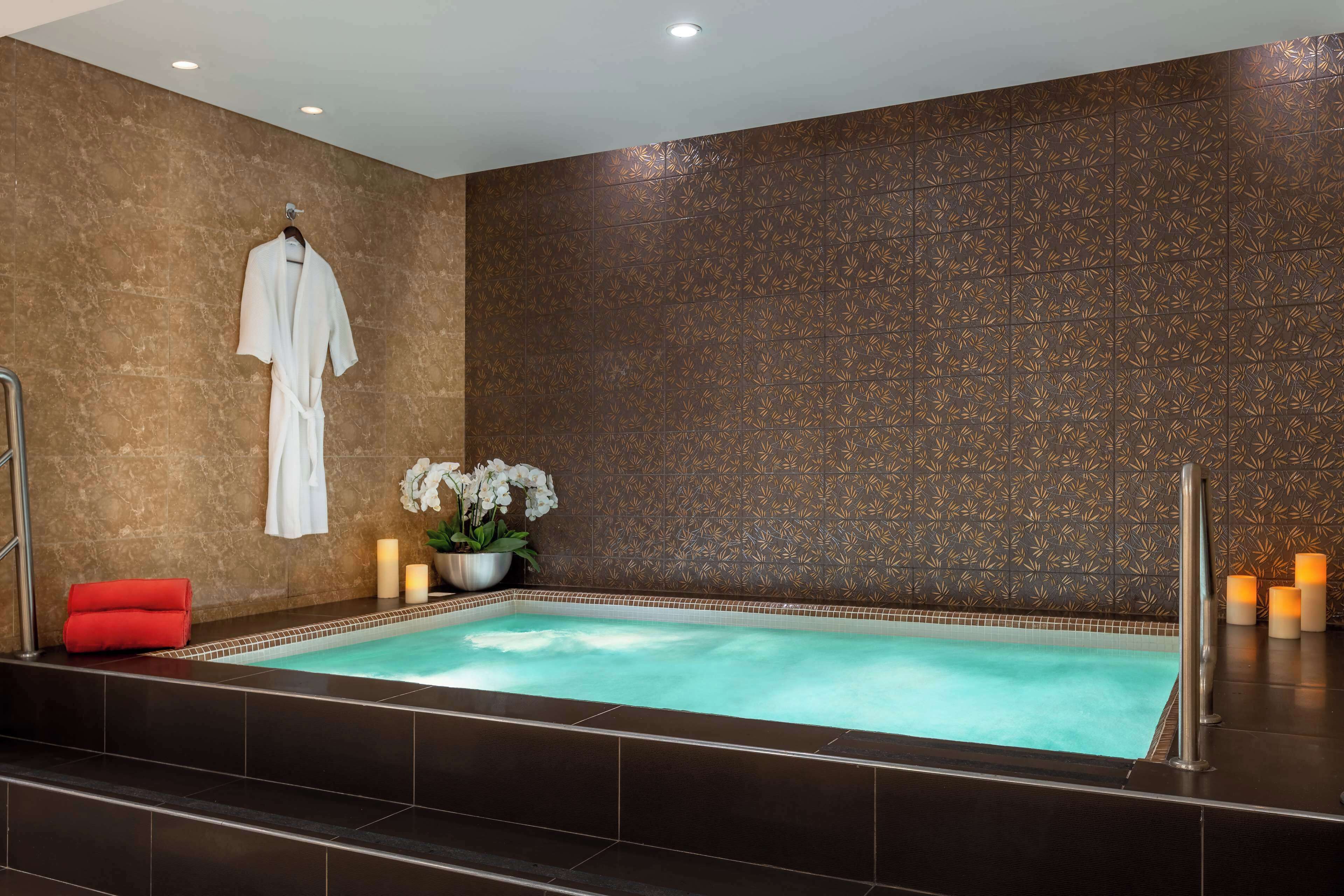 A spa area with a hot tub, a robe hanging on a rack, and candles.