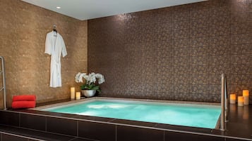 Un área de spa con un jacuzzi, una bata colgada en un perchero y velas.