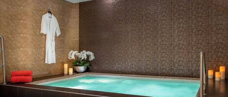 Un área de spa con un jacuzzi, una bata colgada en un perchero y velas.