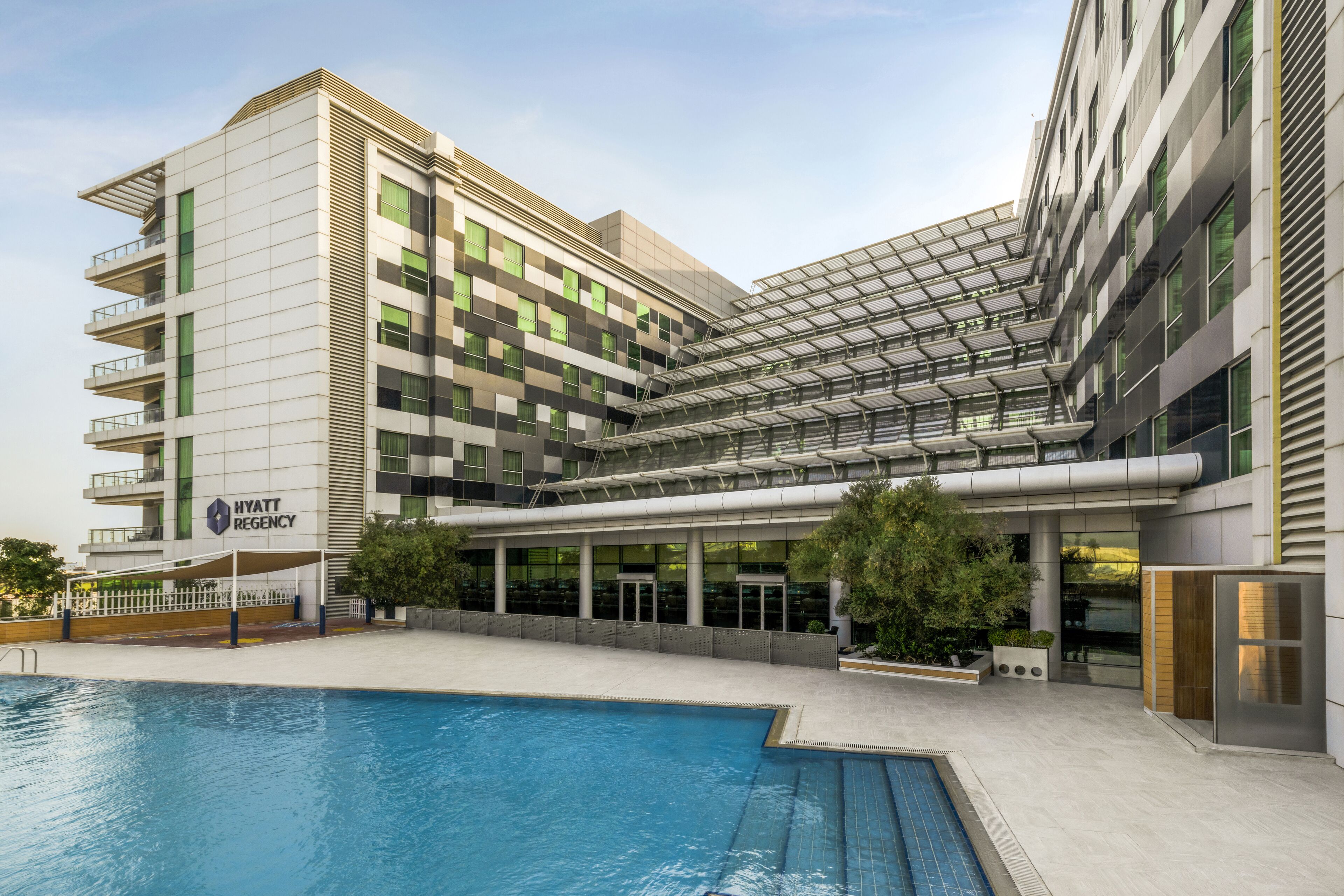 A modern hotel with a pool, a covered outdoor area, and a glass facade.