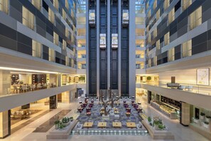 Un moderno vestíbulo de hotel con varios pisos, un espacio central abierto con asientos y diversas comodidades, incluyendo un restaurante y un bar.