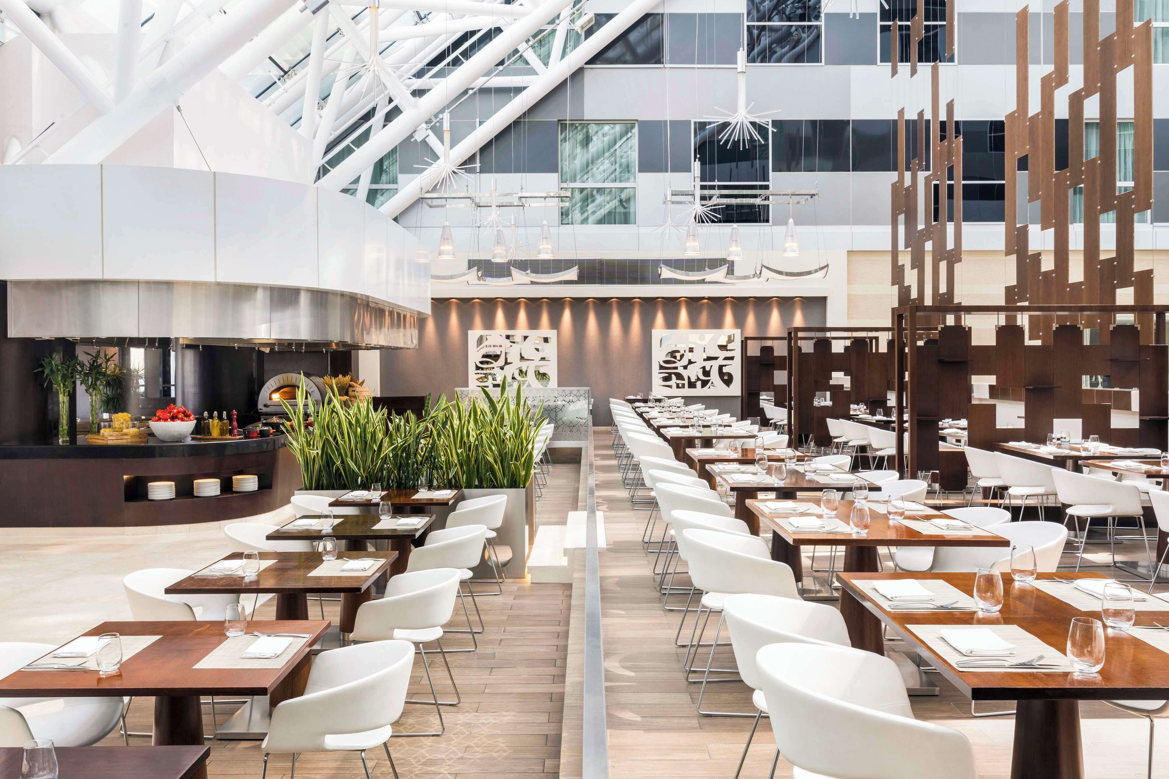 A modern restaurant with a central bar, white chairs, and a long dining table.