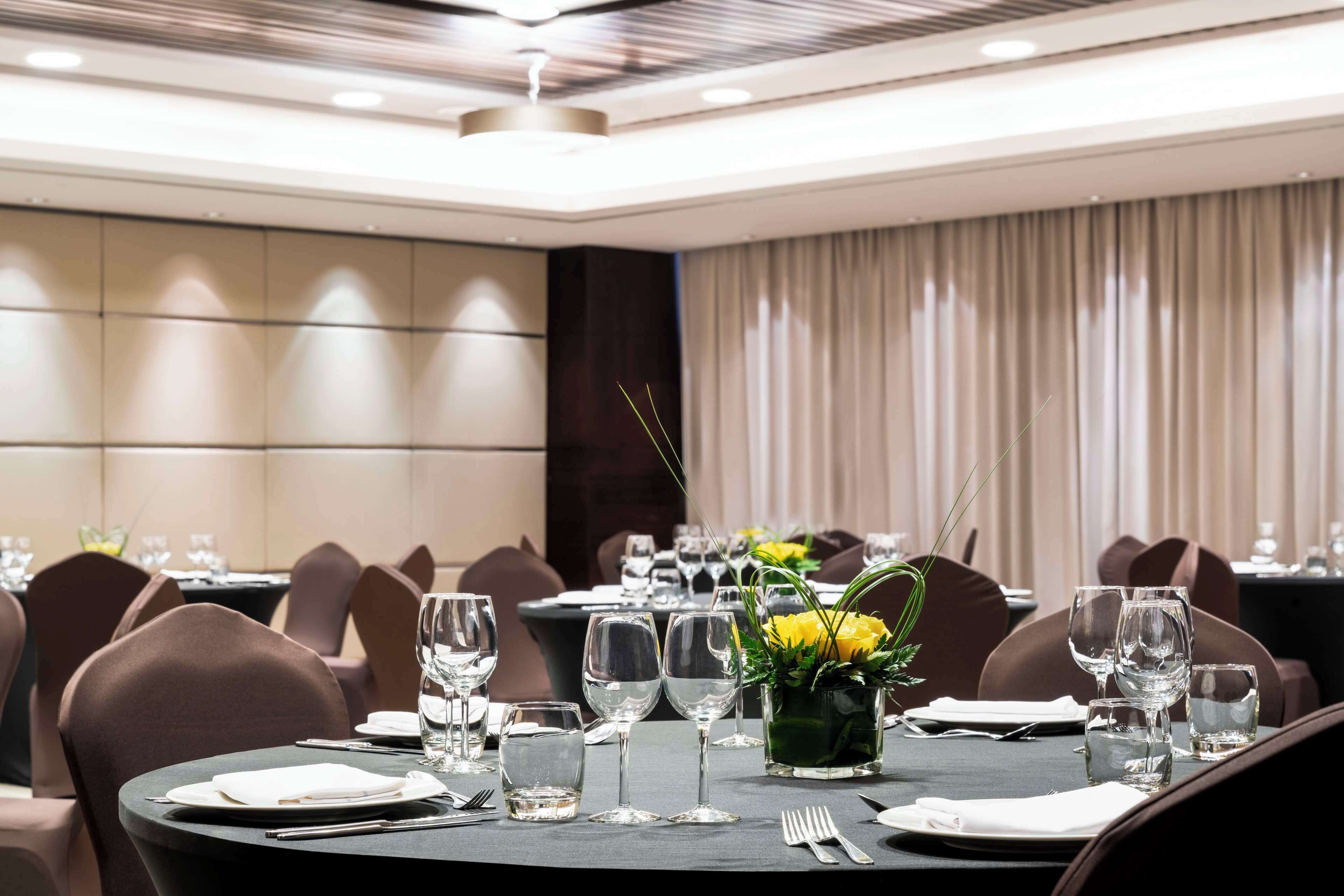 A well-lit dining area with round tables set for a meal, featuring clear glassware and a centerpiece with yellow flowers.